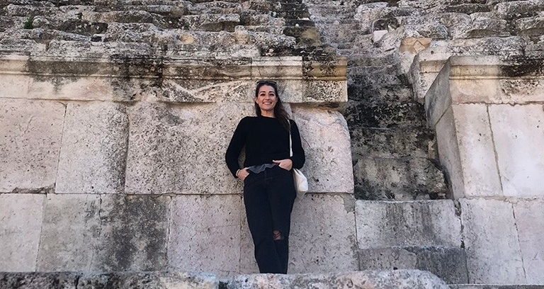 Hannah stands in ront of a a huge wall of rock and stone.