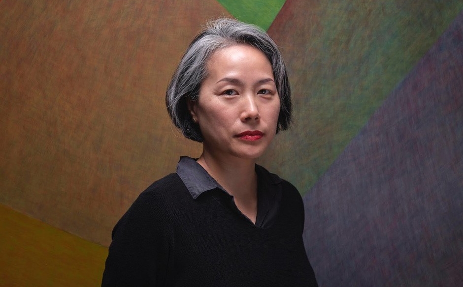 Jinny stands in front of her abstract paintings which is multicoloured muted tones.