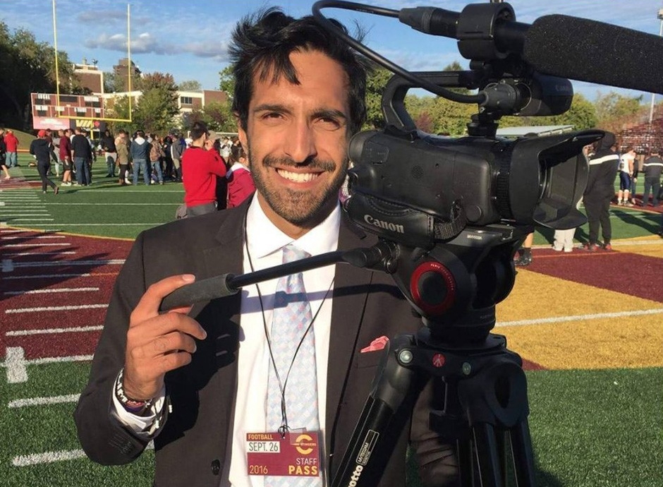 Salim stands behind a television camera on the football field at Concordia's Loyola Campus.
