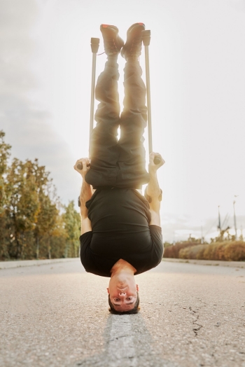 Break dancer Luca Patuella balances on his head in the middle of a road lined by trees.