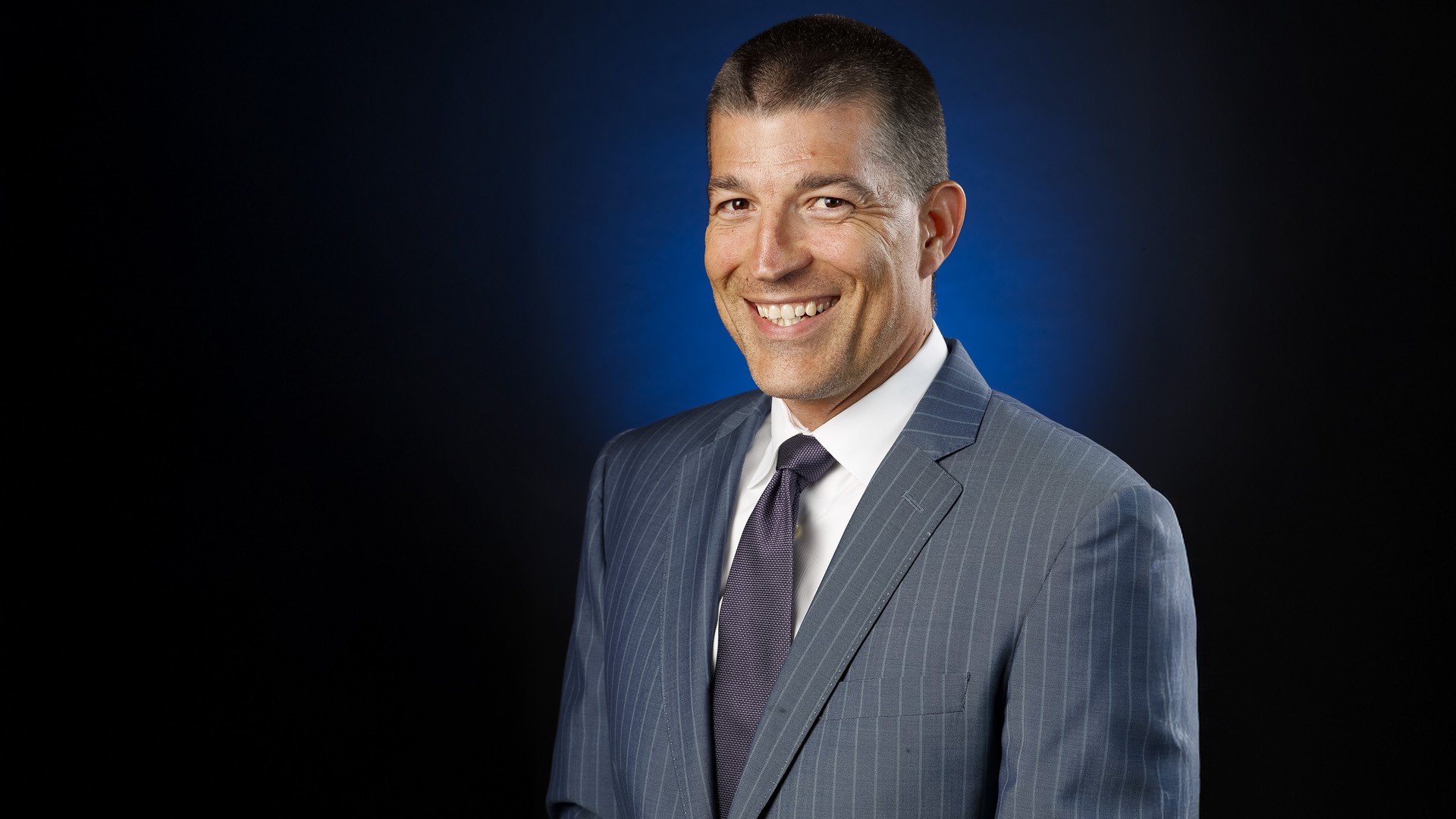 Julien BriseBois, EMBA 07 Julien has very close cropped hair and wears a blue suit and navy tie.
