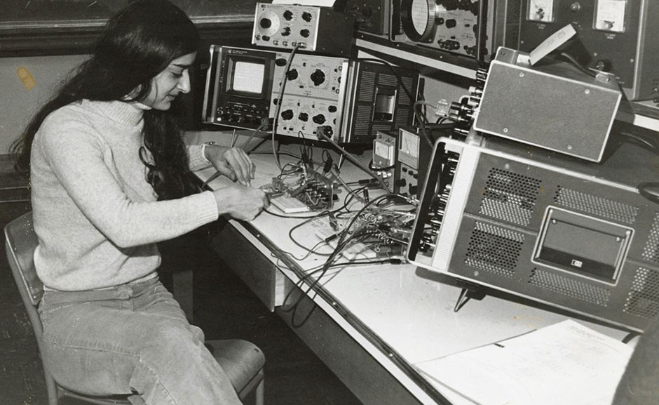 A woman with long dark hair is working with wires that are attached to computer equipment.