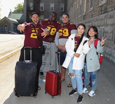 Three Stingers football players wear their jerseys next to two students who have just moved in to residence.