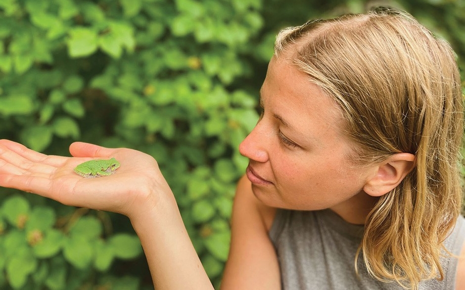 Sophie looks at a tiny frog she holds in her hand.