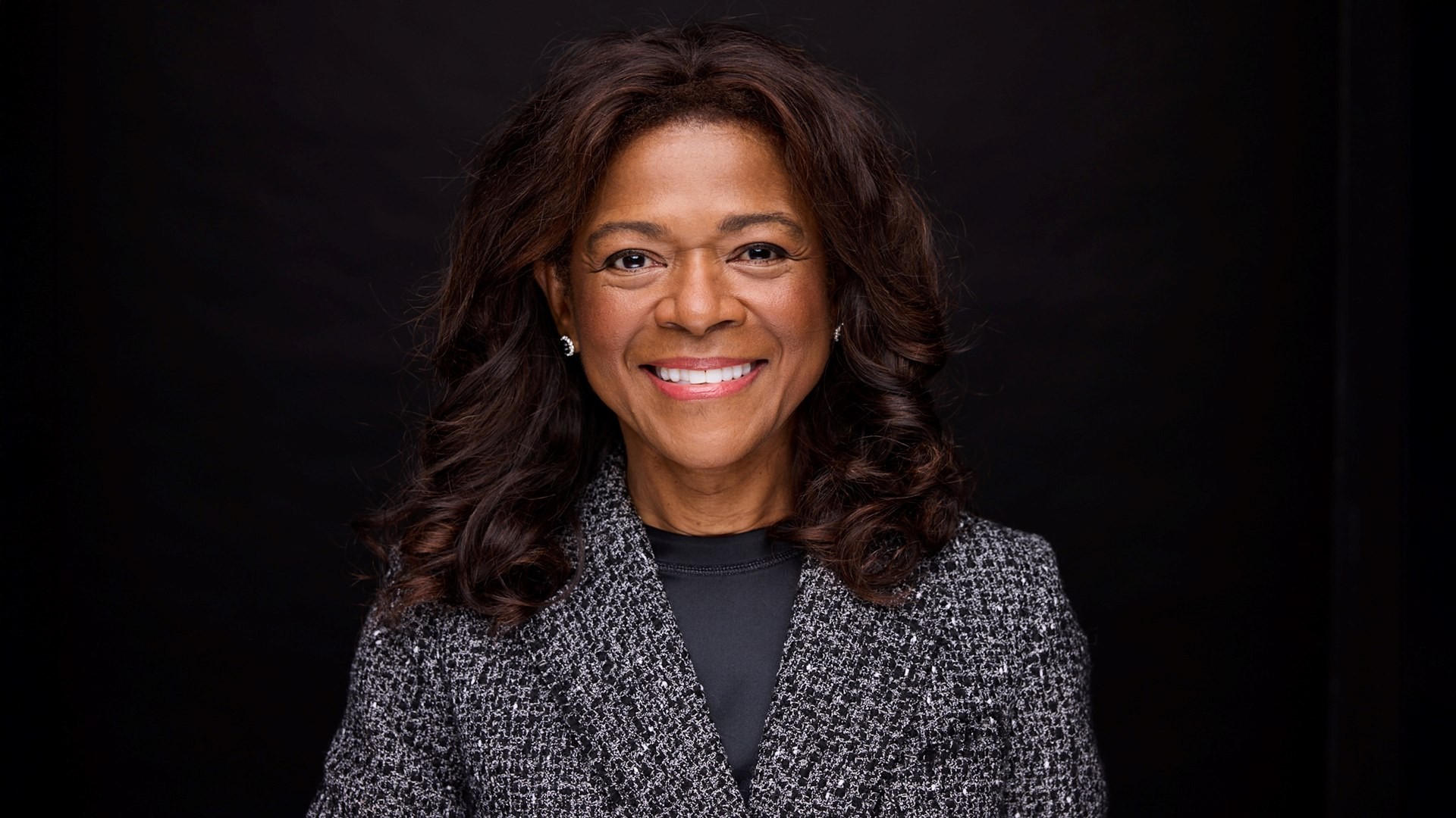 A smiling woman wearing a tweed blazer looks at the camera.