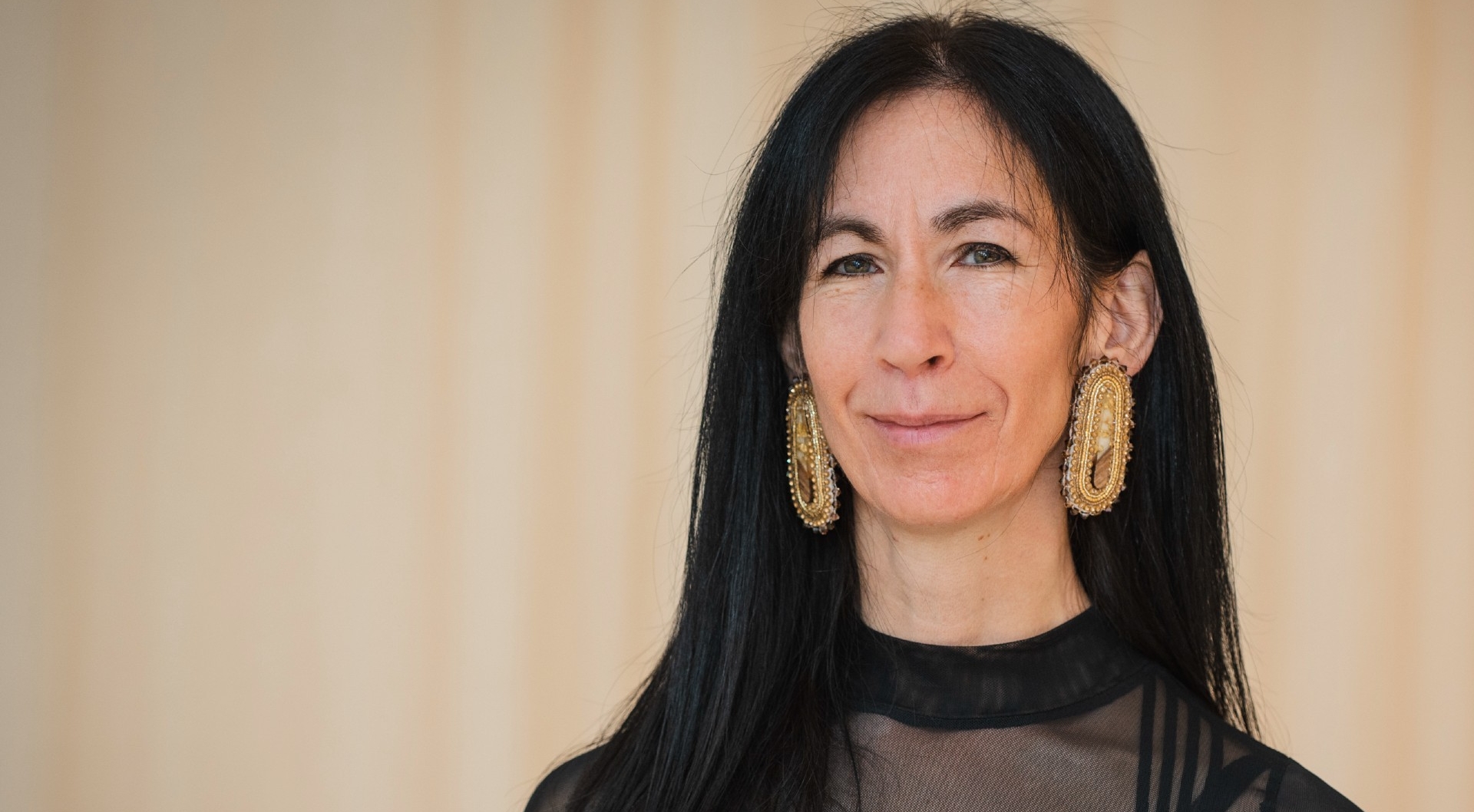 A headshot of Barbara who has long black hair and is wearing large gold beaded earrings. earrings