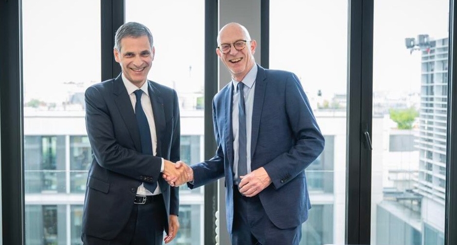 Two men in business suits smiles broadly while shaking hands.