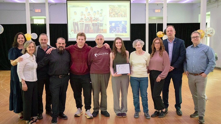 Eleven people are standing in a row. One of them is holding a certificate. Behind them a screen shows a slide show.
