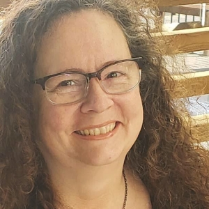 The late Chantal Boucher is smiling and has long, curly brown hair and wears glasses.