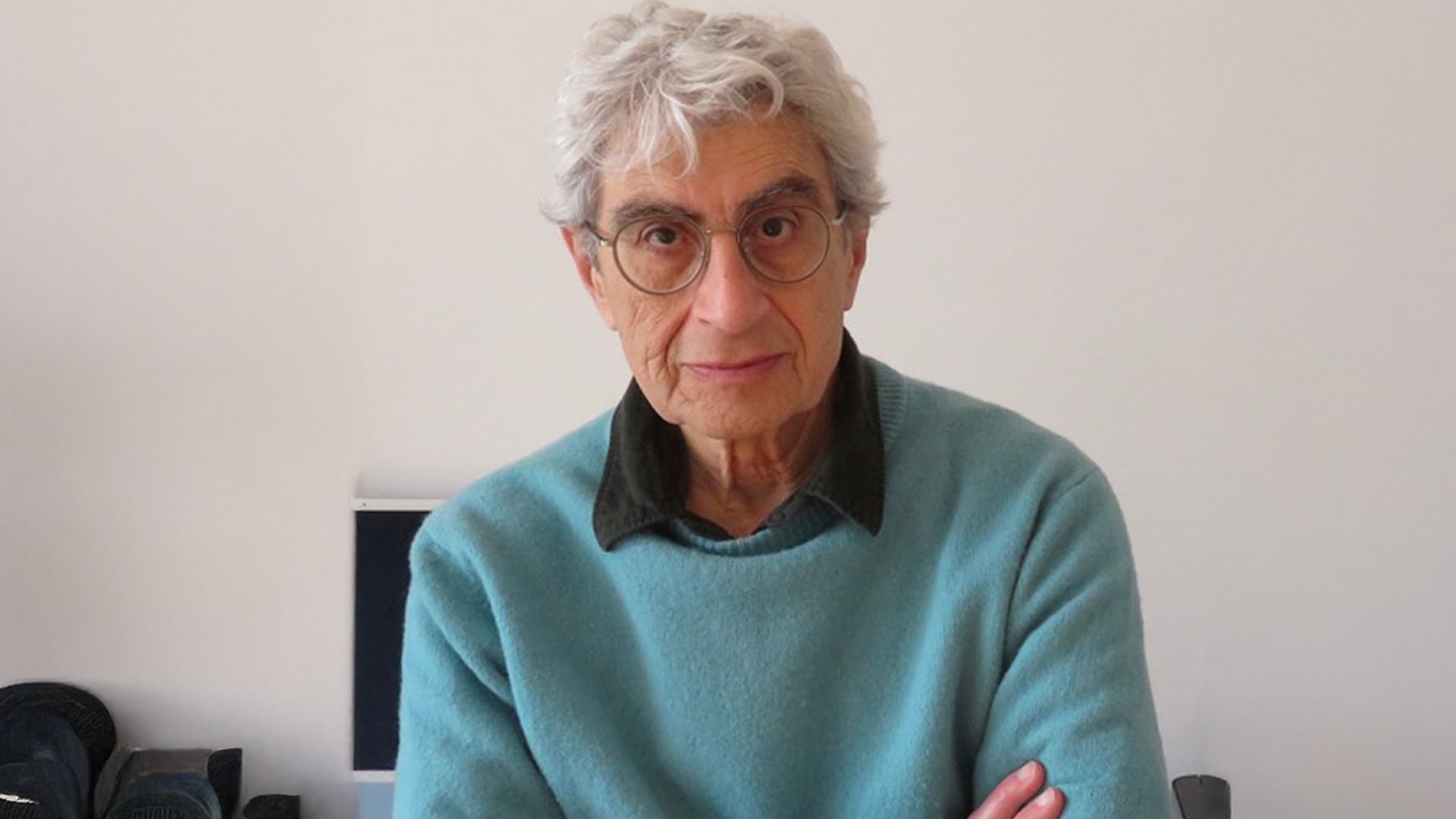 Pan has grey hair and glasses. He wears a pale blue sweater over a black shirt.