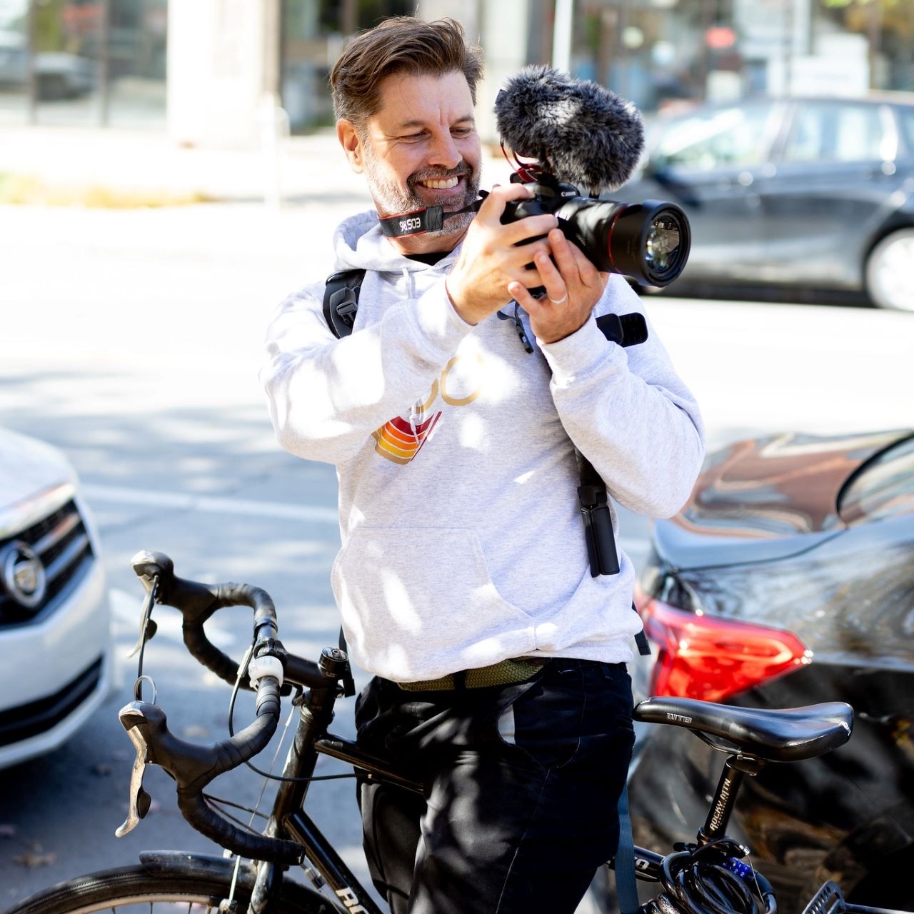 Photographer on a bike A man in a hoodie holds up a camera while sitting atop a bicycle.