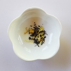 White bowl with scalloped edge with a small amount of water and colored tea leaves at the bottom