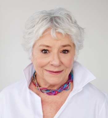 Woman with white hair, wearing a white blouse and colorful necklace, against a white background.