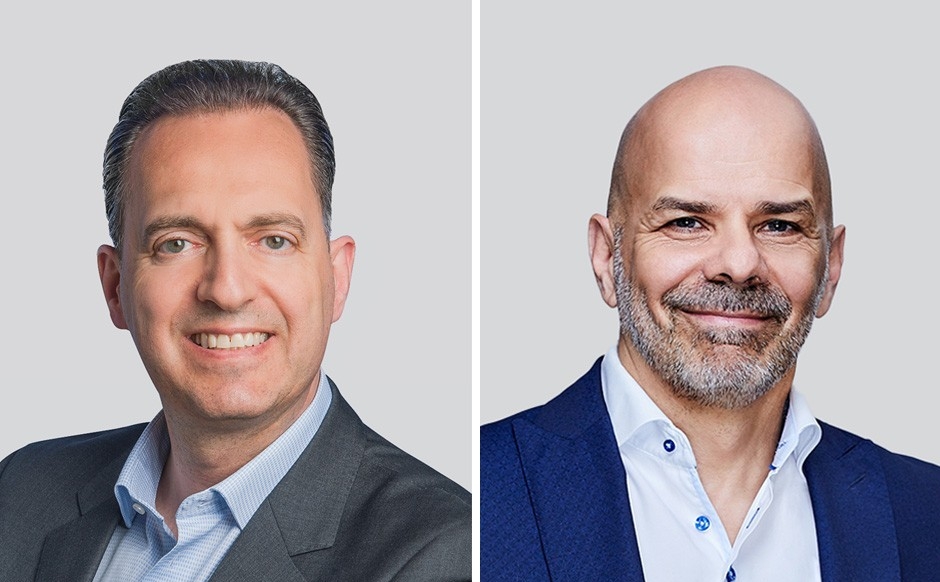 Headshots of 2 businessmen wearing suits and blue shirts with no tie.