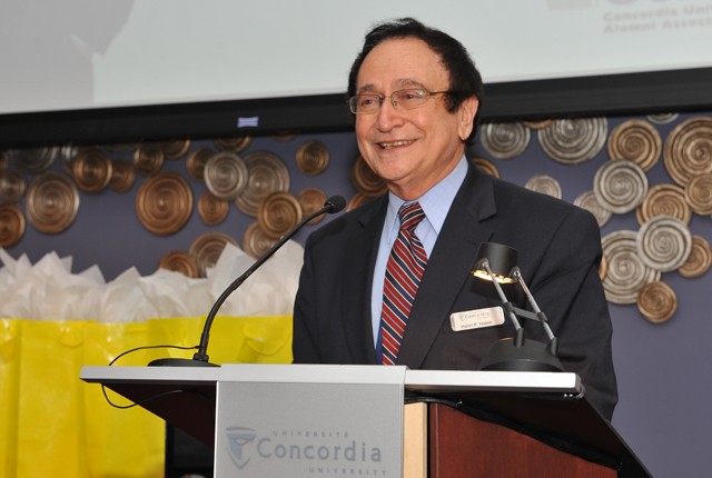 A man in a suit and tie speaks at a Concordia-branded podium.