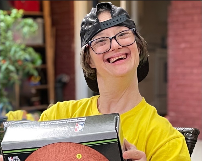 Hannah wears a yellow T-shirt and holds up a basketball.