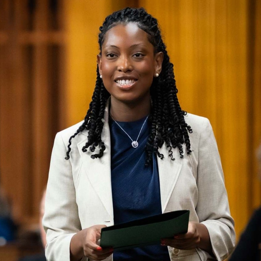 Tatiana Auguste wears a white suit with a blue blouse and holds a folder.