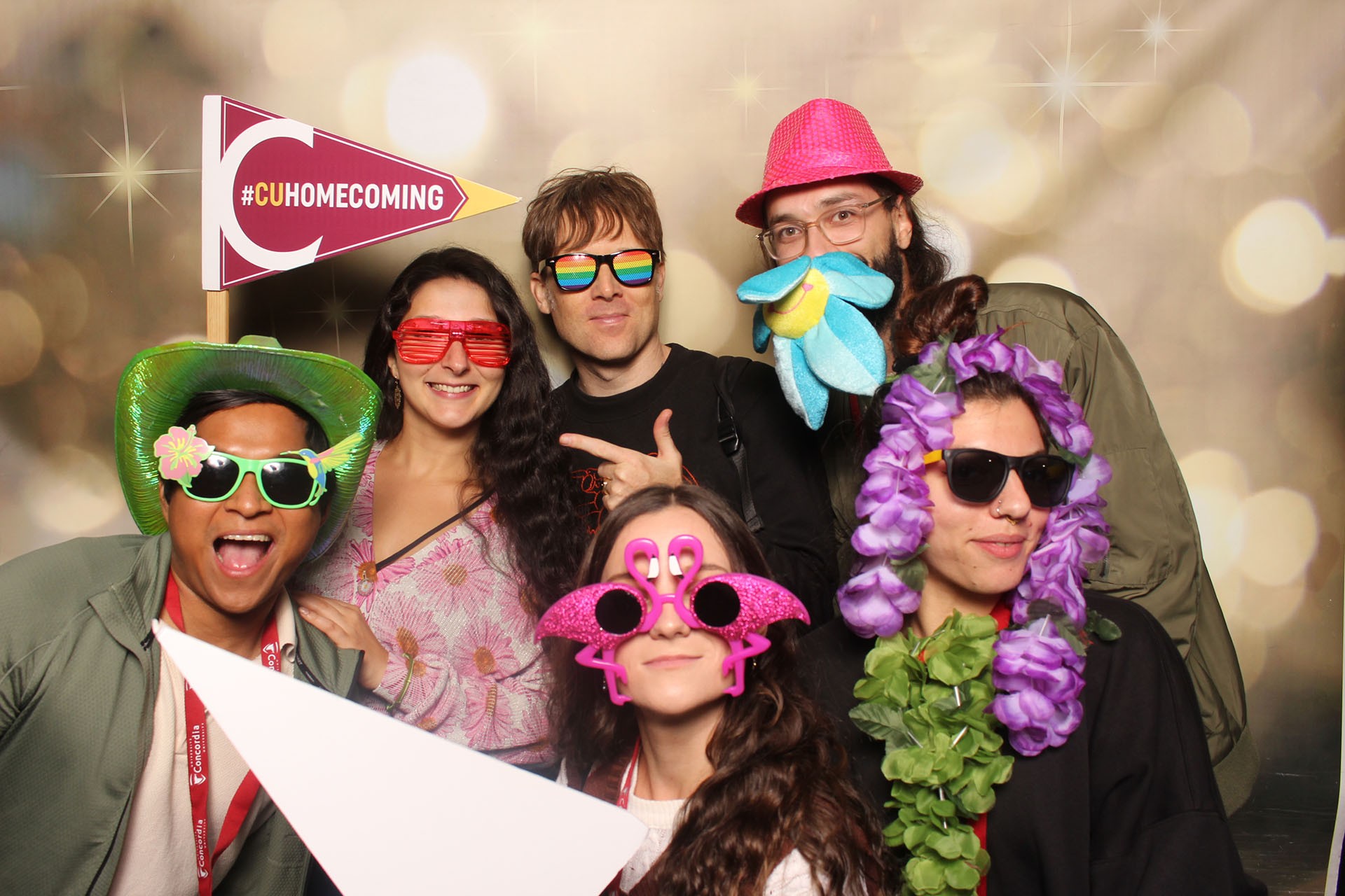 Six people pose in a photo booth with colourful props and Homecoming signs.