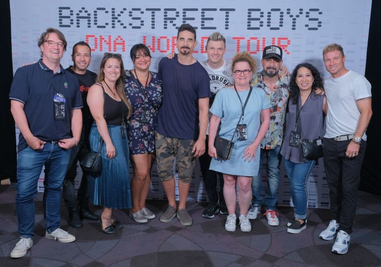Ten people stand in a row in front of a banner that says Backstreet Boys DNA World Tour.