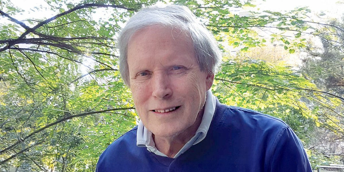Ian MacDonald is outside in front of trees and wearing a navy blue sweater over a collared shirt. 