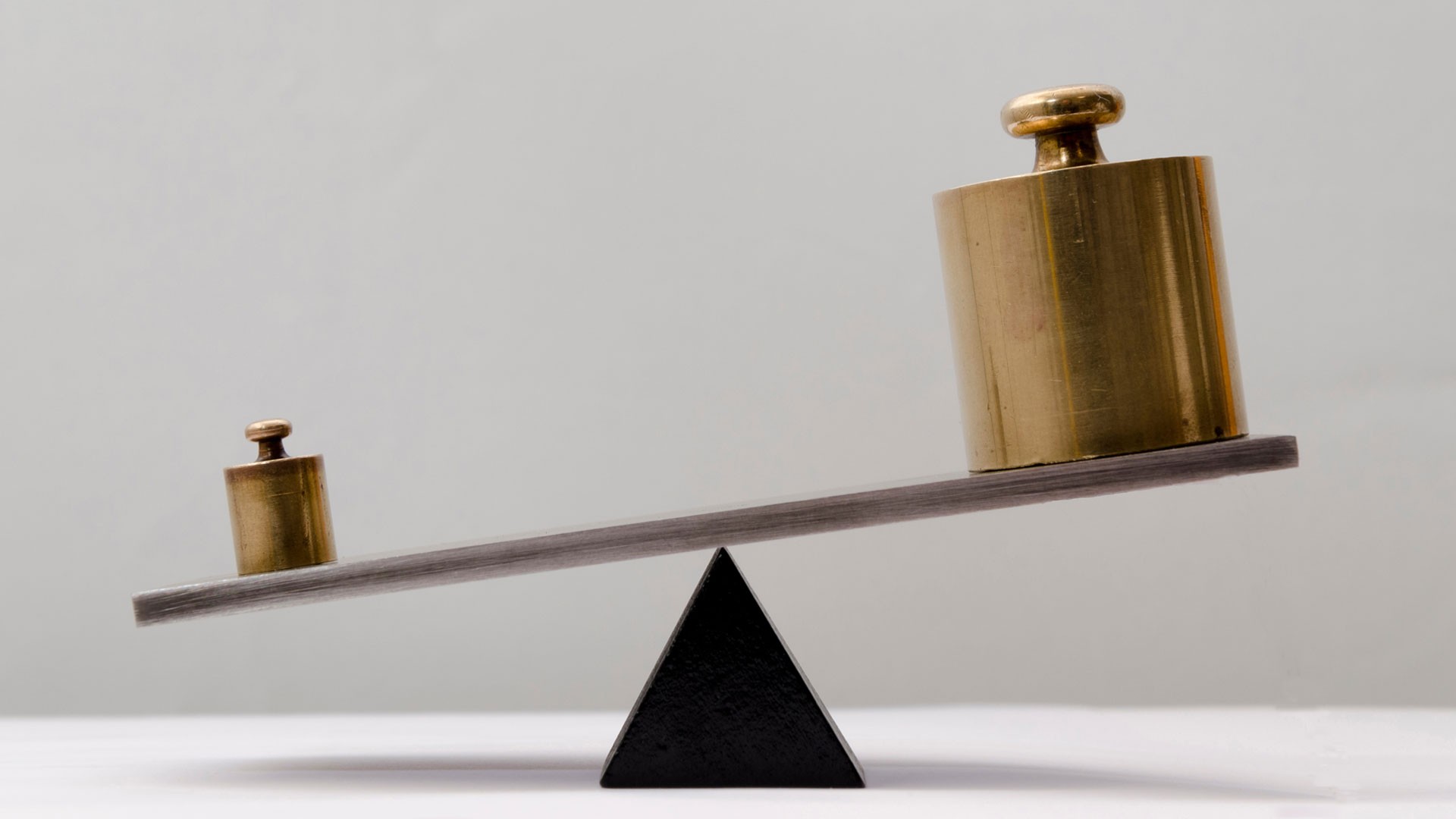 Two small weights on a scale whereby the smaller one seems to weigh less than the larger one.
