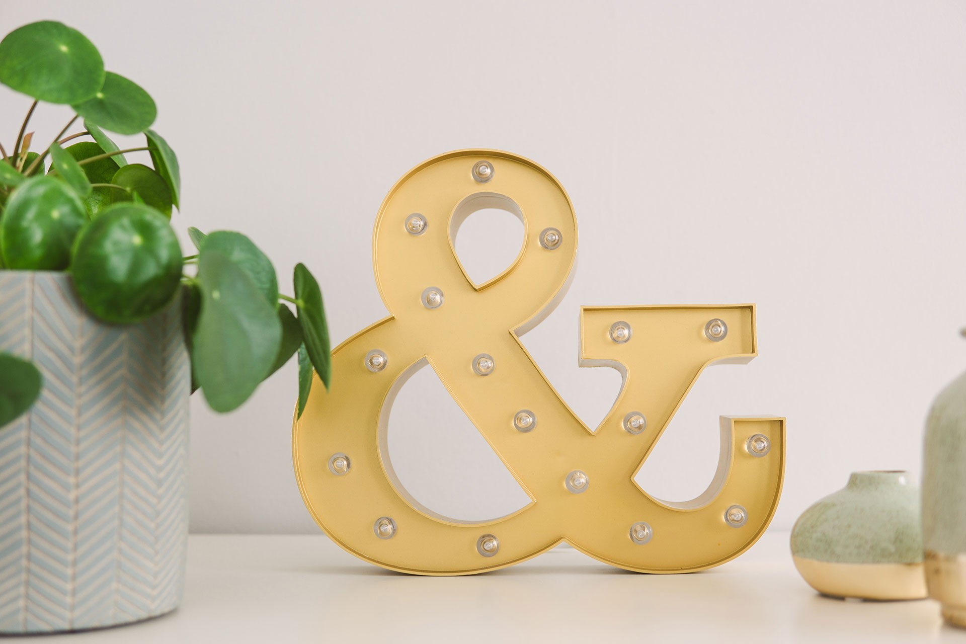 Illuminated ampersand symbol on top of a table next to plants in pots