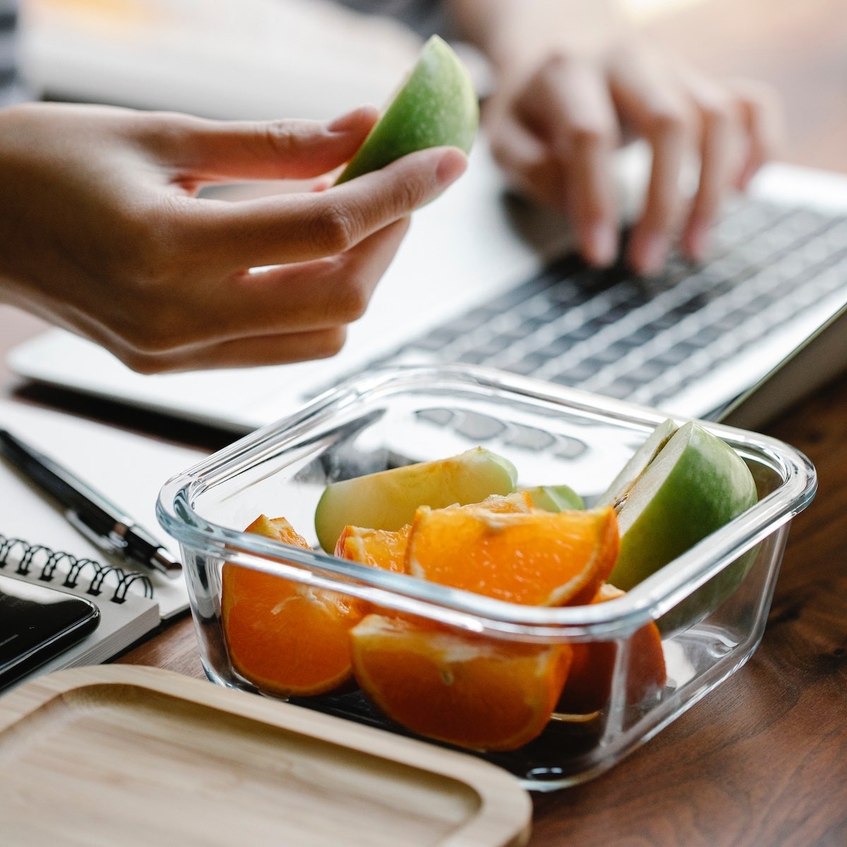 Person eating oranges and apples from a container, while using their laptop