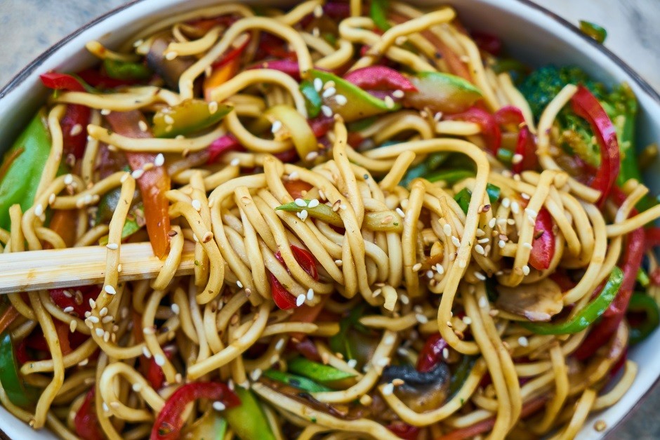 Chopsticks in a bowl of noodles and stir-fried veggies