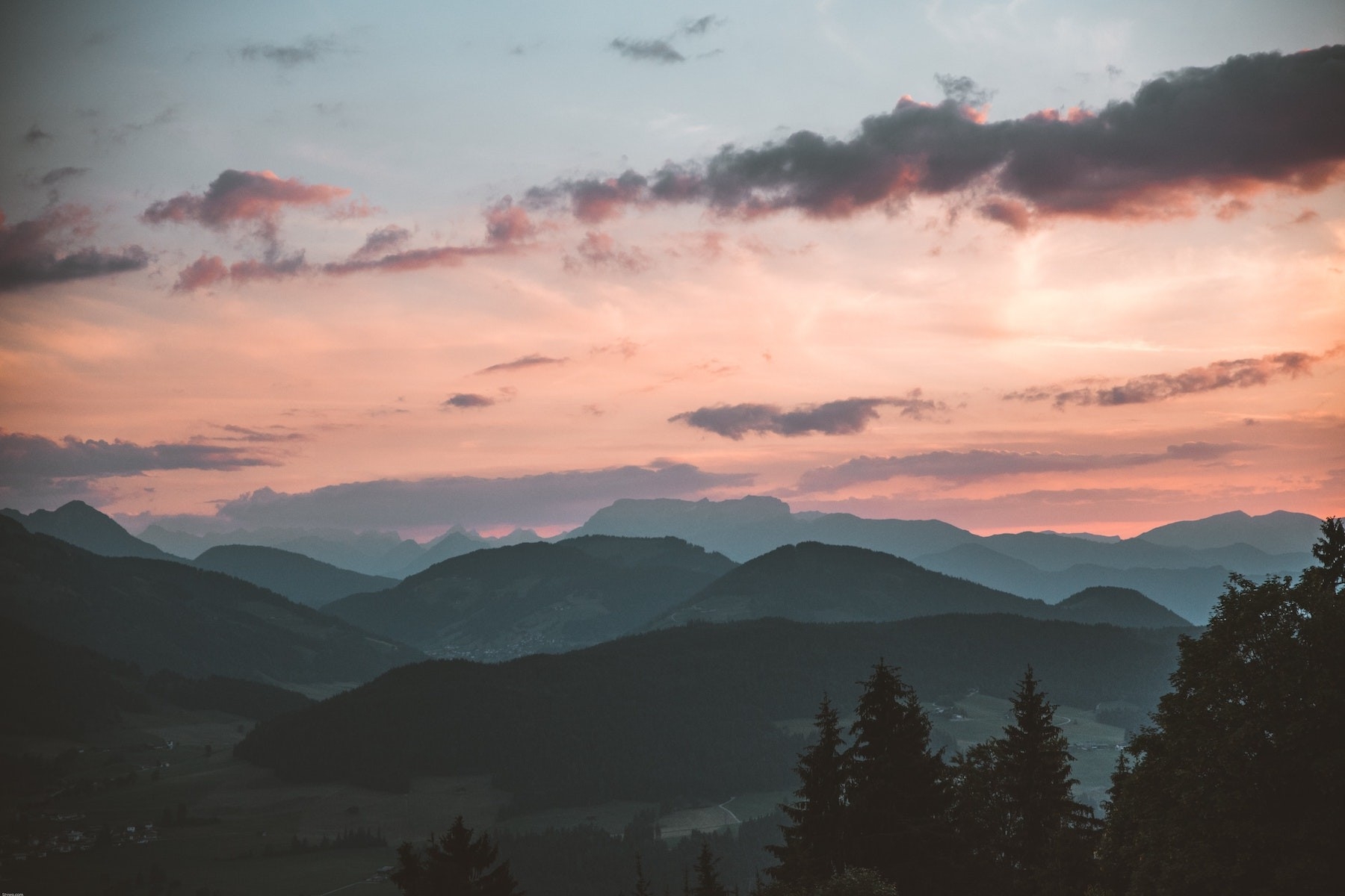 A sunset with mountains, trees and pink clouds