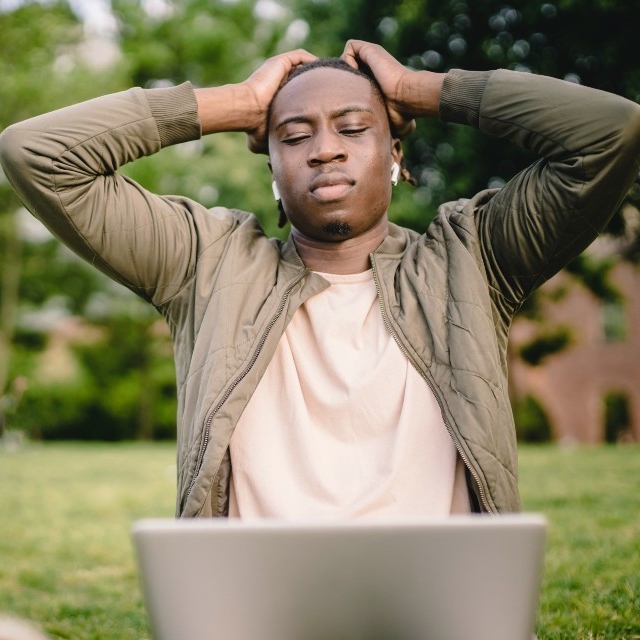 A stressed man sits outside with a laptop and holds his head