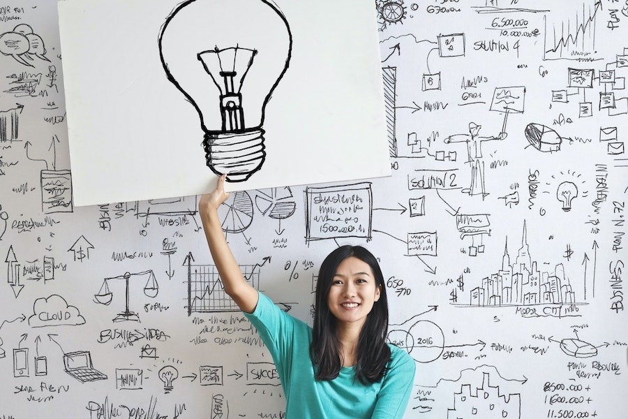 woman holding a photo of a light bulb on a doodled background