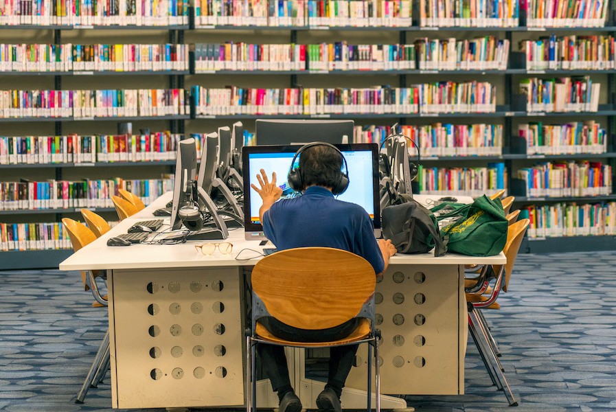 teacher sitting in a library in front of a computer