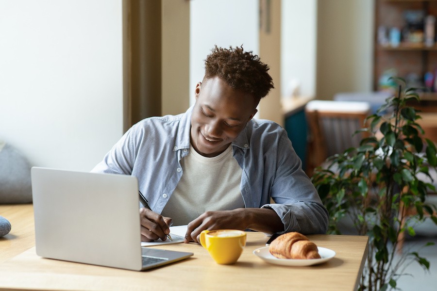 a person writing in a notebook in front of a laptop in a soothing place