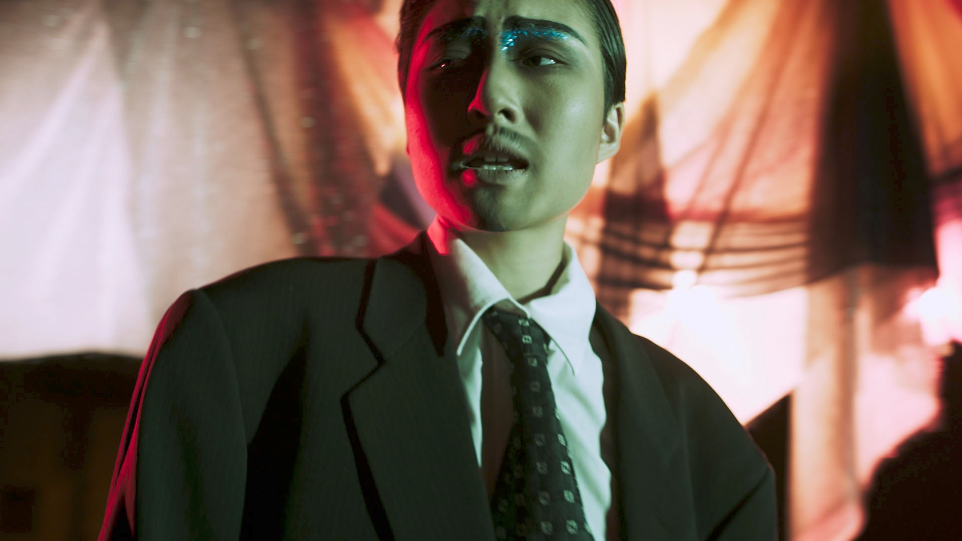 siren eun young jung An gender non-conforming Asian person wears blue glittery eyeshadow and has a mustache.