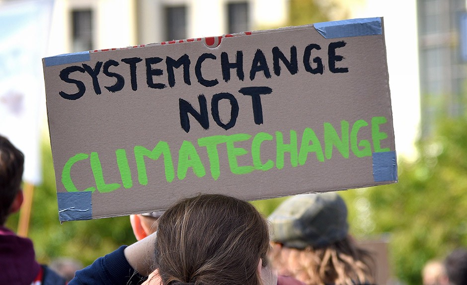 n a demonstration, person holding a poster with slogan "System change not Climate change"