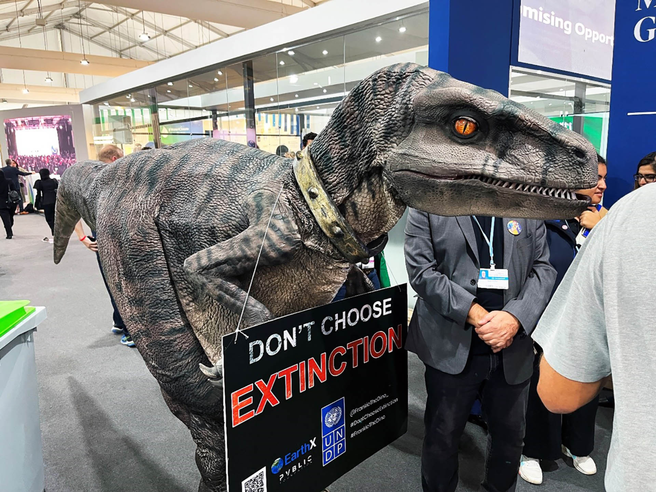 A photo from inside a pavilion hall with a dinosaur costume warning of the potential extinction due to climate change.