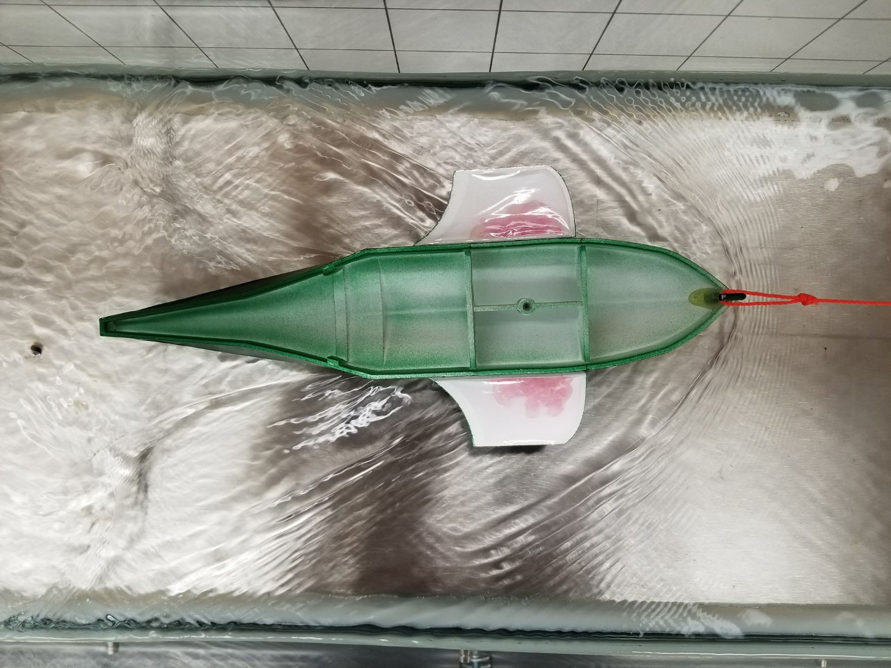 The image shows a small-scale green 3D printed hull floating in water during a water test from the 2017-2018 AERO490 multidisciplinary aerospace capstone group at Concordia University for their light amphibious aircraft design.