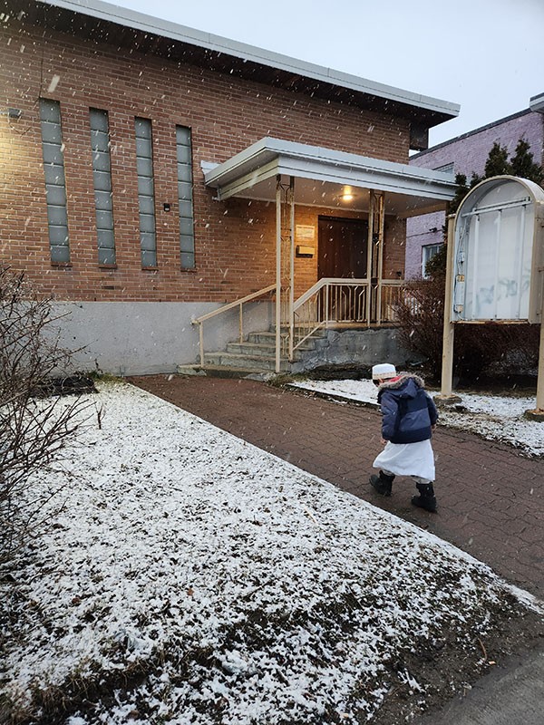 Child walking while snow lightly falls around him.