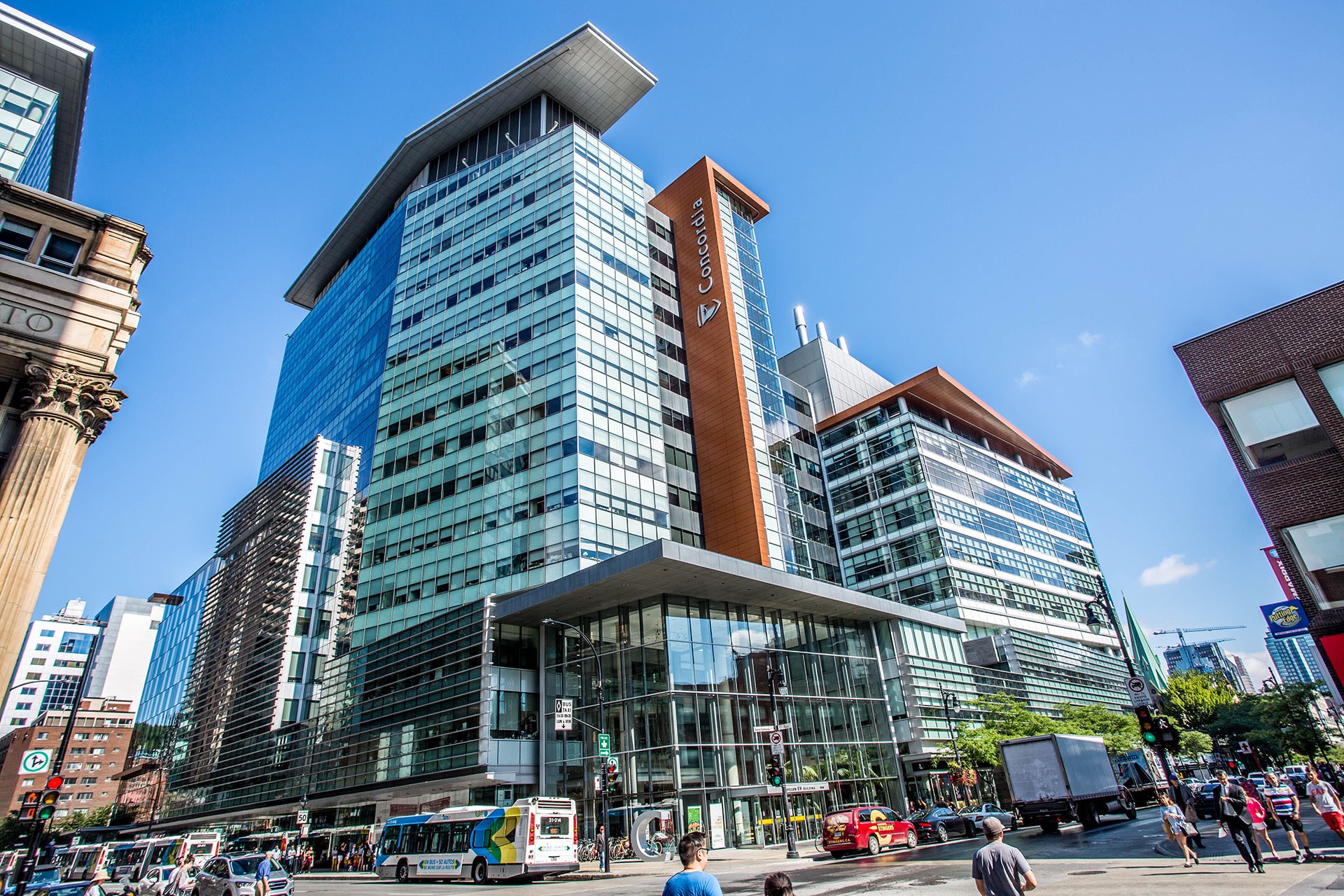 Le bâtiment EV de Concordia par une belle journée ensoleillée avec des étudiants marchant et des bus urbains garés