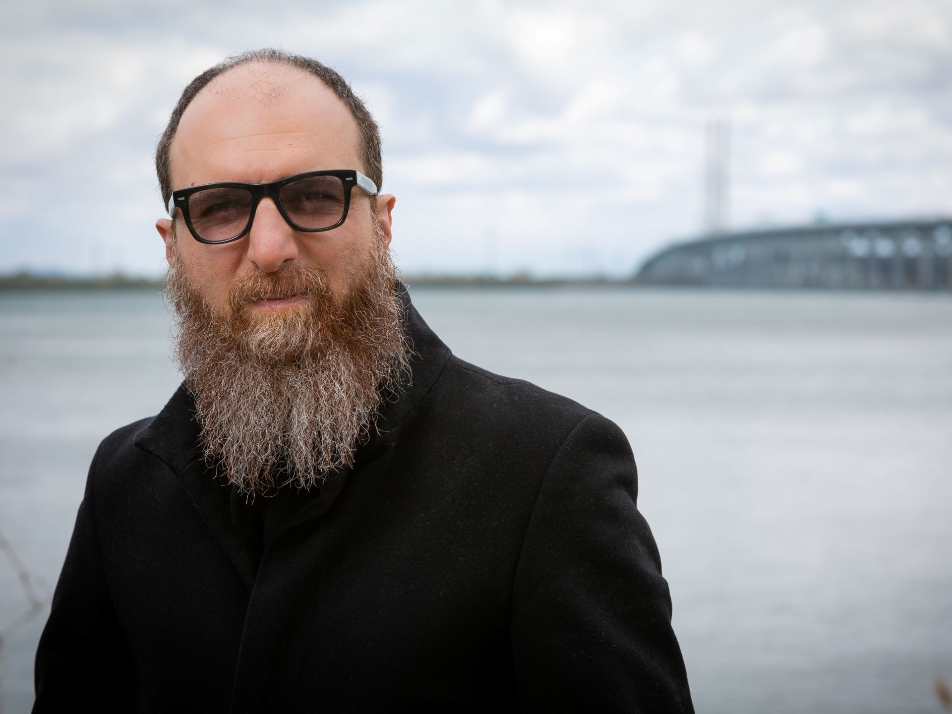 Bearded man in dark glasses standing by the St. Lawrence River