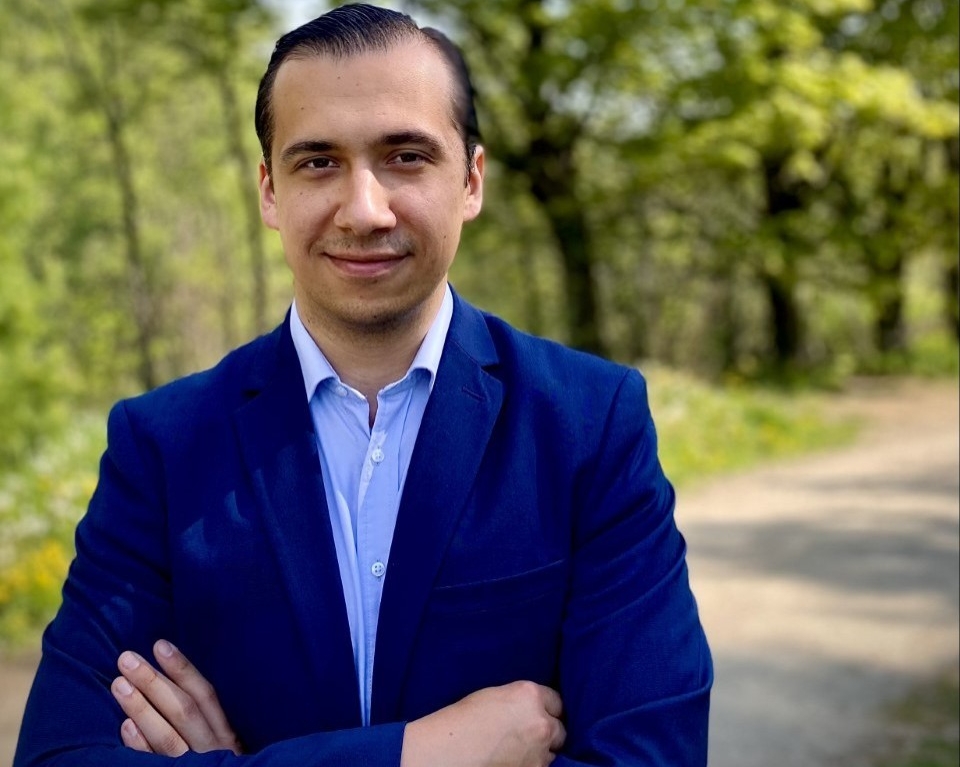 Man in blue jacket standing by a tree-lined road