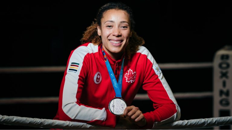  Femme souriante portant une fermeture éclair rouge avec une feuille d'érable canadienne et le logo des Jeux olympiques, tenant une médaille.