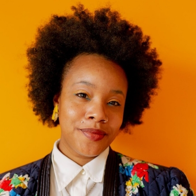 Femme aux cheveux courts portant un chemisier boutonné blanc et un blazer noir et fleuri coloré