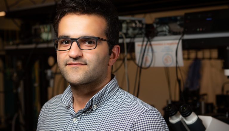 Man with dark hair and glasses standing in a lab