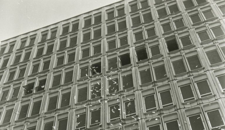 Photo en noir et blanc prise en regardant un bâtiment de la ville avec de petits morceaux de papier voletant des fenêtres supérieures.