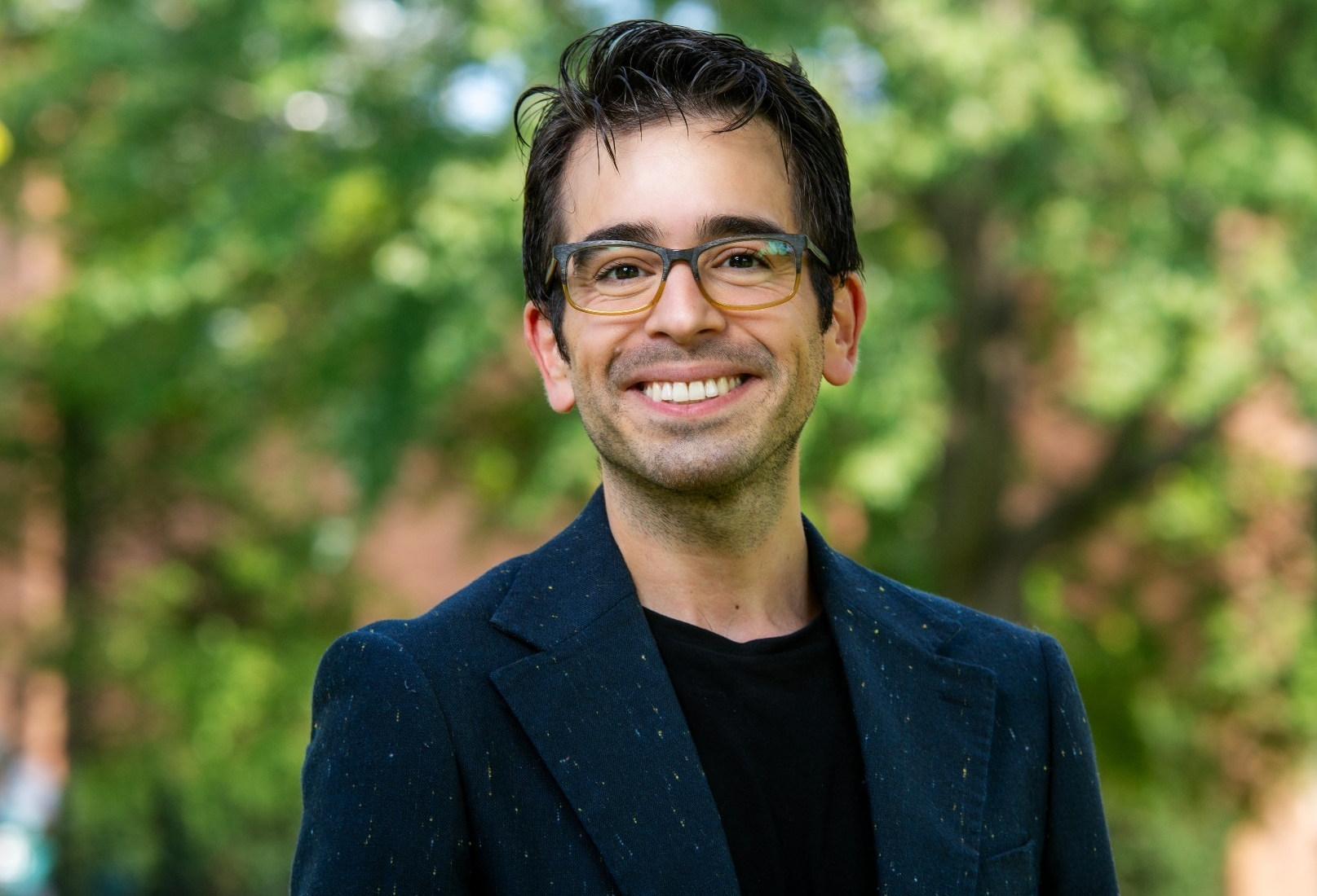 Nicolás Alessandroni porte une chemise noire, une veste bleue et des lunettes.