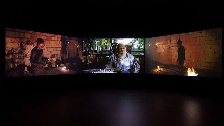 Image cinématographique d'un intérieur sombre avec deux personnages et un feu ouvert.