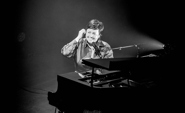 Ariane Moffatt : « Composer des chansons est un outil formidable pour canaliser positivement cette intensité et pour se découvrir en tant que personne. » Image en noir et blanc d'une jeune femme souriante aux cheveux courts et foncés, assise à un piano à queue.