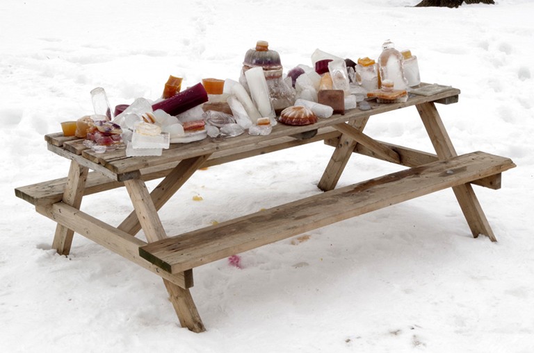 Une table de pique-nique en plein air dans la neige, avec des sculptures de glace et d'agar-agar sur le dessus.