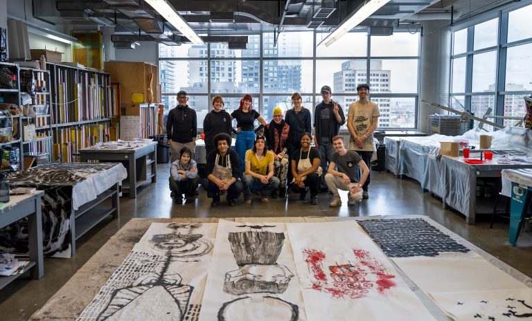 Un groupe de personnes regroupées dans un grand atelier d'art et souriant à l'appareil photo.